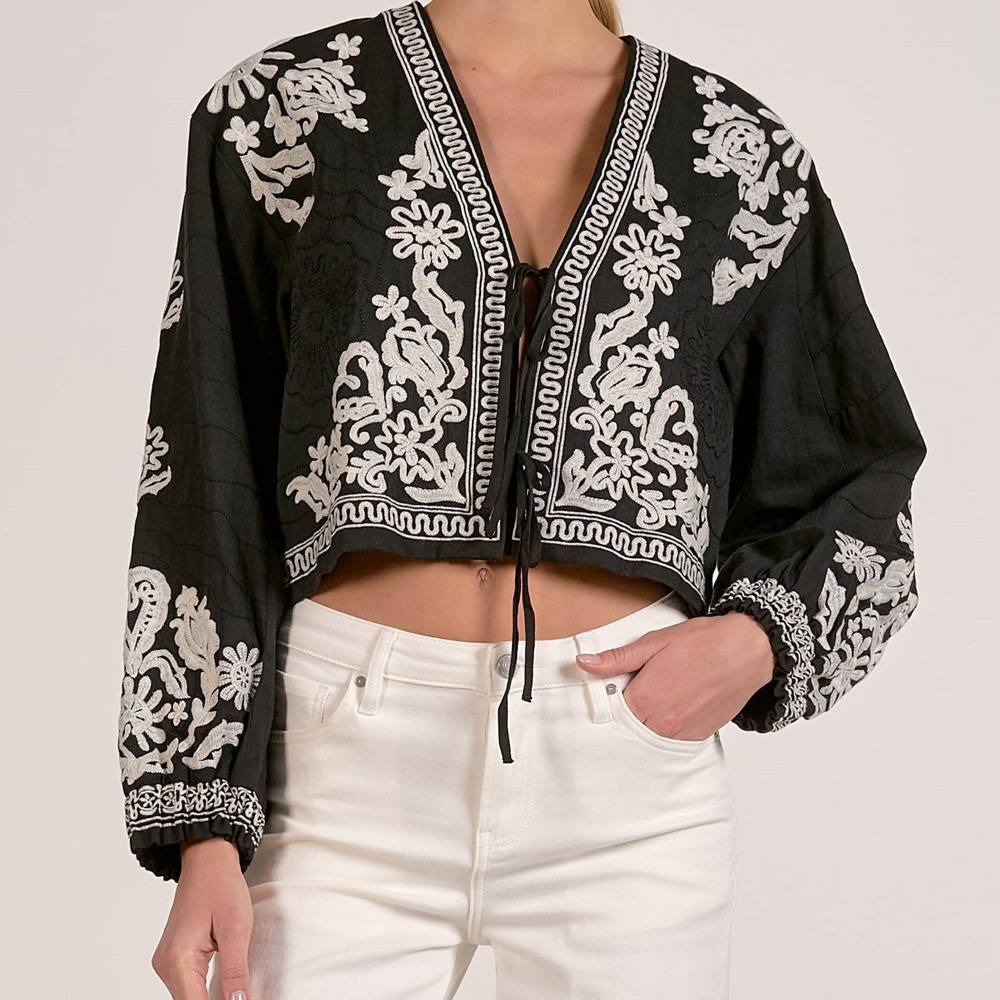 Black embroidered top with white patterns worn by a person on a plain background