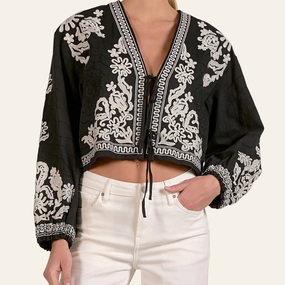 Black embroidered top with white patterns worn by a person on a plain background