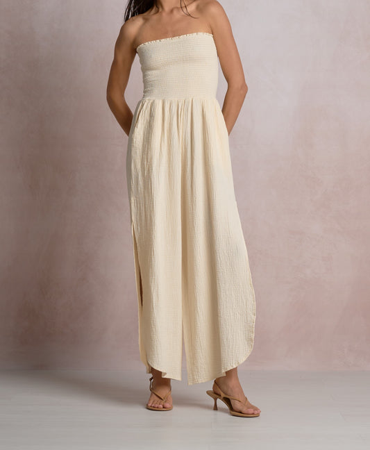 Woman wearing a strapless, long beige dress against a plain background