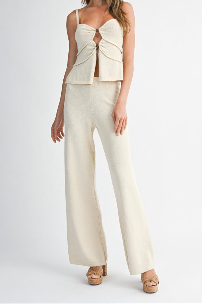 Woman wearing a cream-colored outfit with a top and wide-leg pants on a white background