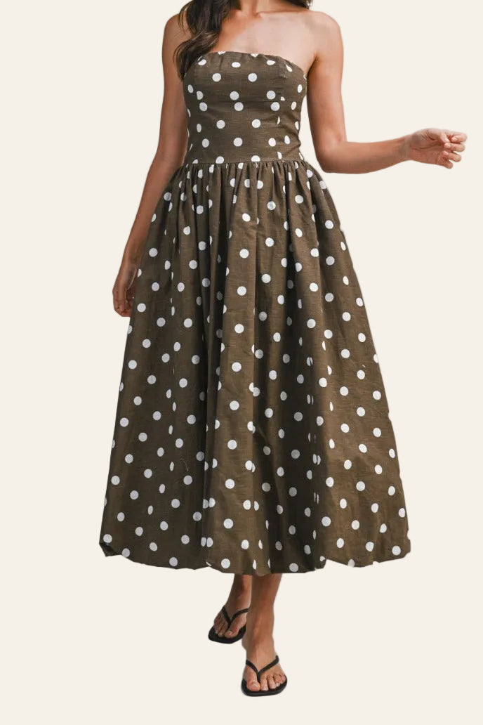 Woman wearing a strapless brown dress with white polka dots on a gray background