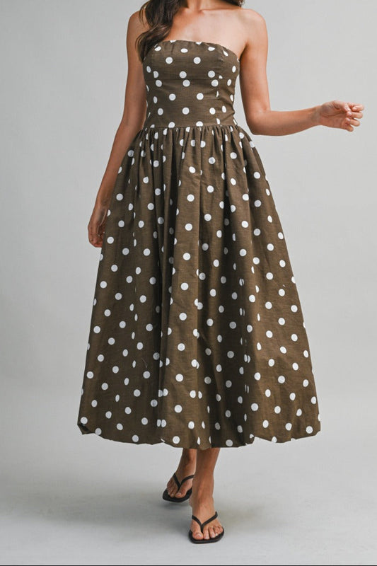 Woman wearing a strapless brown dress with white polka dots on a gray background
