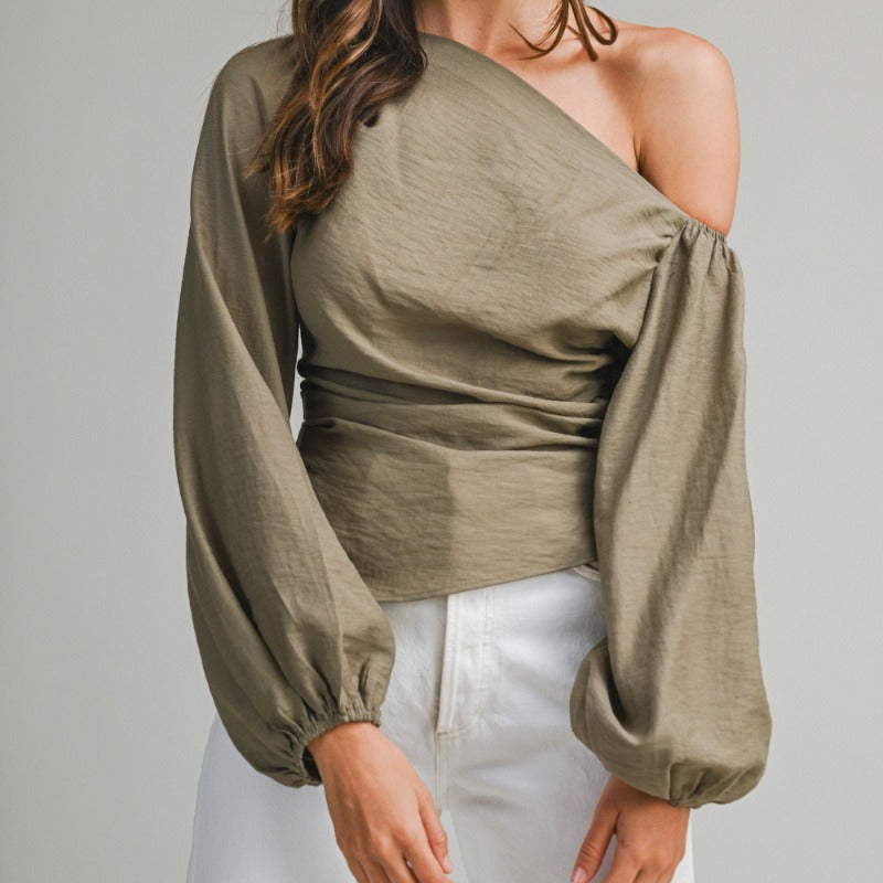 Woman wearing a green one-shoulder top with long sleeves on a plain background